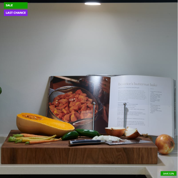 Wooden cutting board with vegetables and an open cookbook on a kitchen counter.