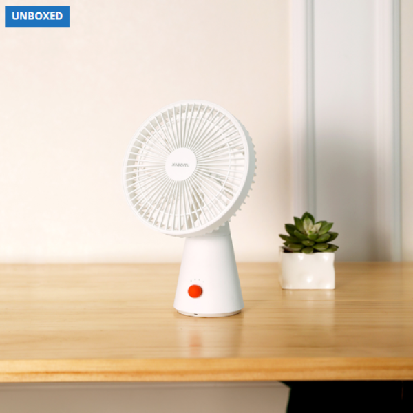 White portable fan on a wooden surface with a plant in the background