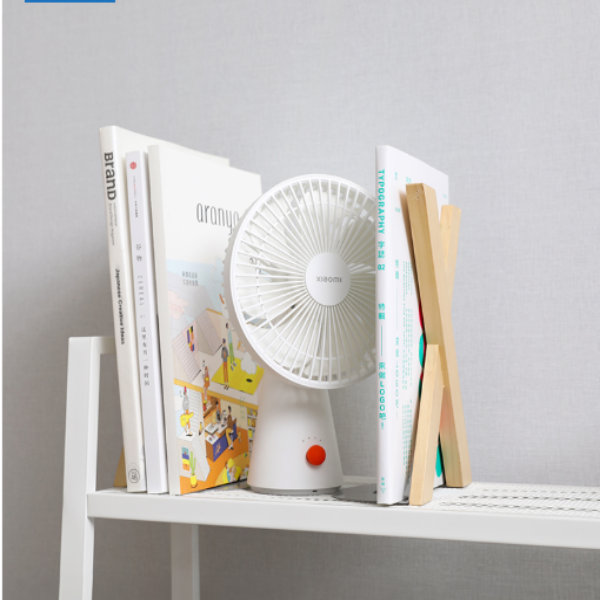 Small white fan placed among books on a white surface with a gray background