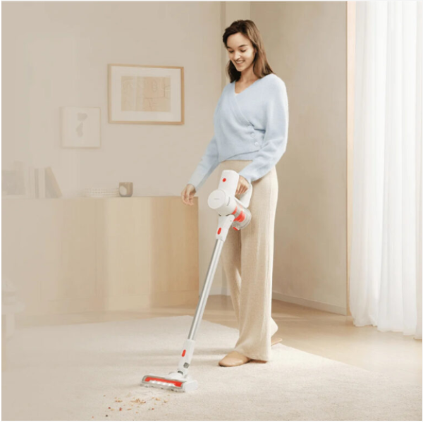 Woman using a vacuum cleaner on a carpeted floor in a room with light-colored walls.