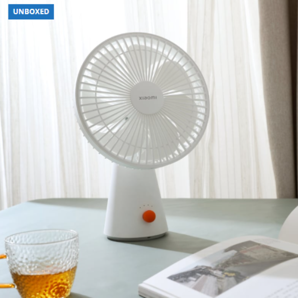 White Xiaomi desk fan on a table with a glass of beer and a book in the background.