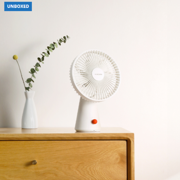 White handheld fan on a wooden surface with a vase and plant in the background