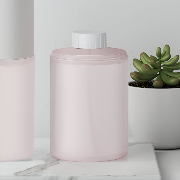 Pink cylindrical container with white cap on a light surface with a plant in the background