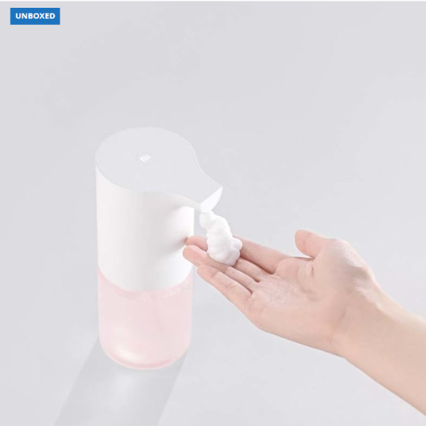 Hand pressing a soap dispenser to release soap onto a hand against a light gray background.