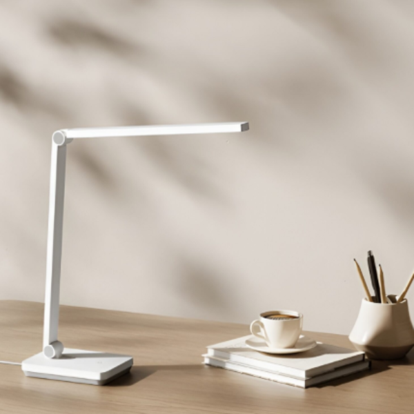White LED desk lamp on a wooden surface with books and a cup.