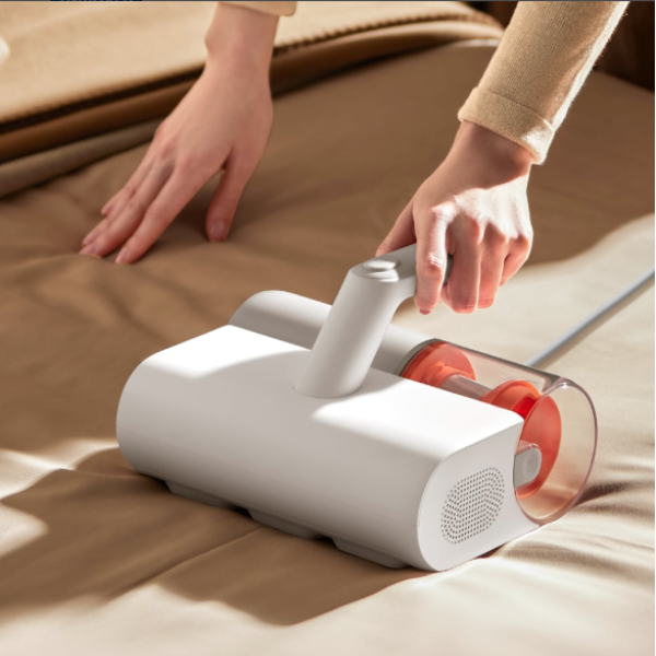 Person using a white handheld vacuum cleaner on a brown surface