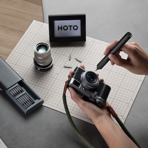 Person holding a camera with tools and a 'HOTO' frame on a grid surface