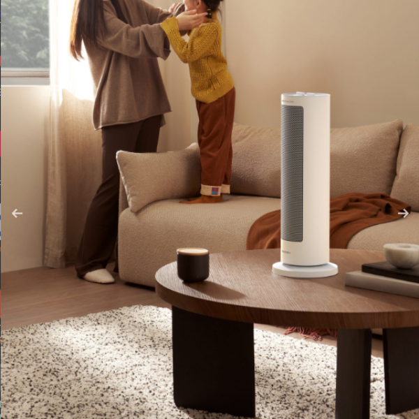 Tall cylindrical air purifier on a wooden coffee table in a living room with a person and child in the background.