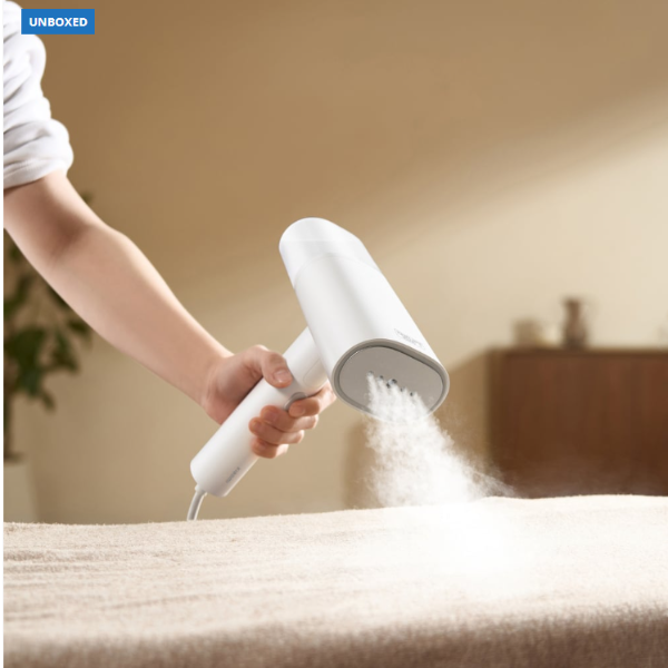 Person using a handheld steam cleaner on a bed with a blurred background