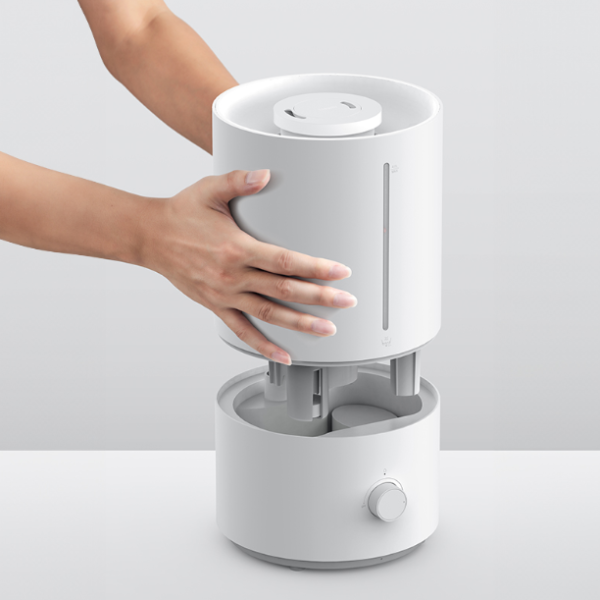 White humidifier with a hand holding it on a light gray background