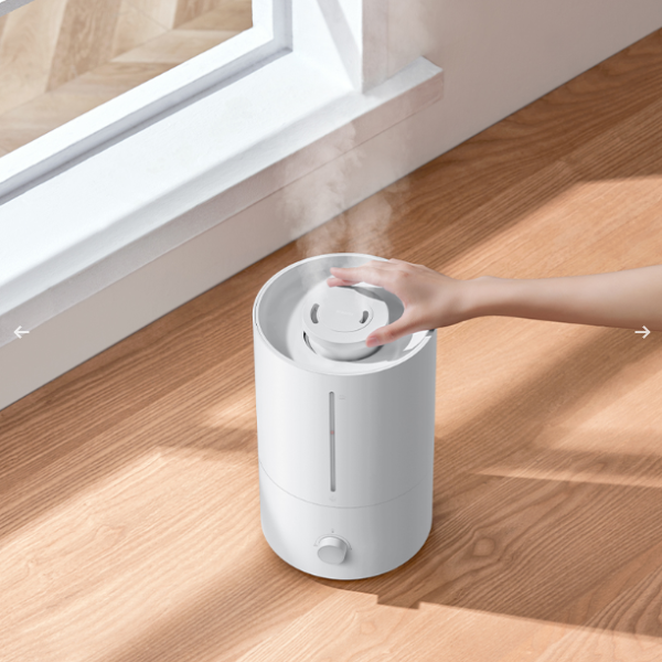 White humidifier on a wooden floor with a hand reaching towards it