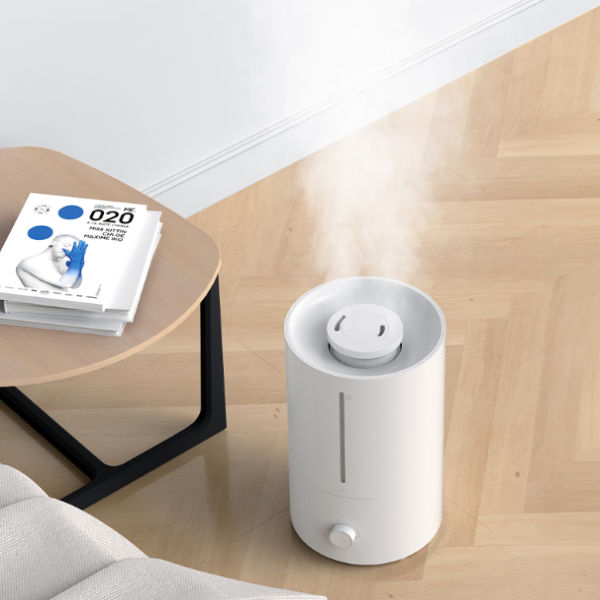 White humidifier on a wooden floor with a side table and books in the background