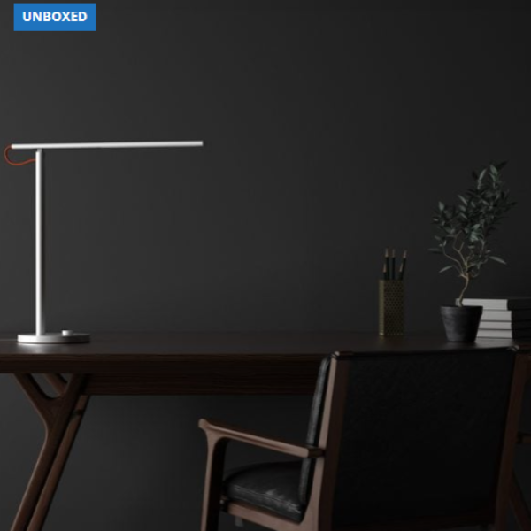 Modern desk setup with a lamp, chair, and minimal decor against a dark wall.