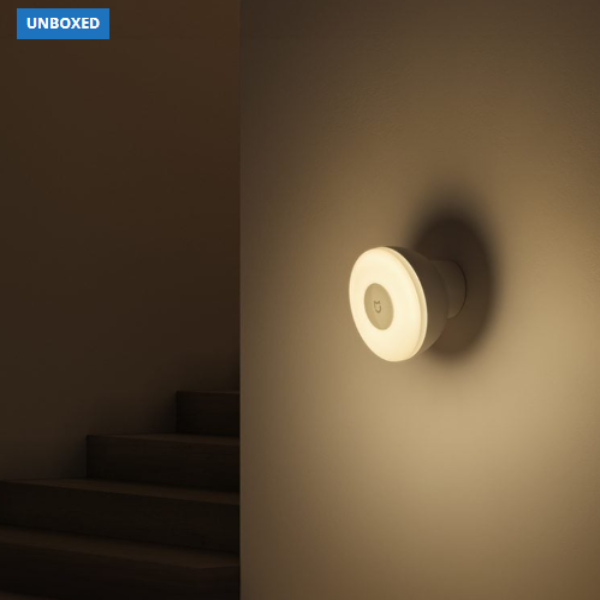 Wall-mounted light fixture casting a warm glow on a wall with a dark staircase in the background.