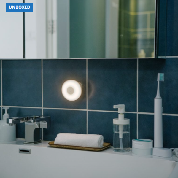 Bathroom setting with a light fixture, toothbrush, and other toiletries on a blue tiled wall.