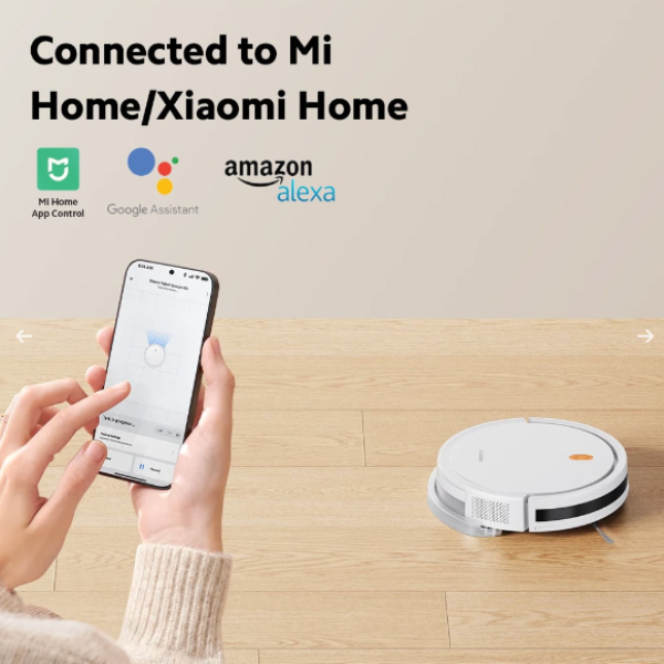 Hand holding a smartphone with app interface, robot vacuum cleaner on wooden floor, and connectivity logos for Mi Home, Google Assistant, and Amazon Alexa.
