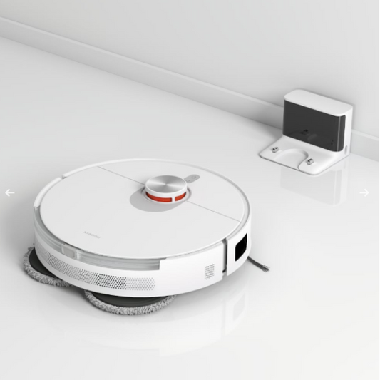 Robotic vacuum cleaner on a white surface with a wall-mounted device in the background