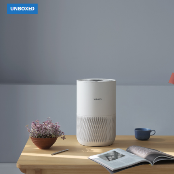 White cylindrical device on a wooden table with a plant, cup, and magazine against a gray background.