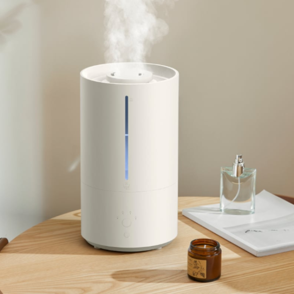 White humidifier emitting steam on a wooden surface with a glass bottle and jar.