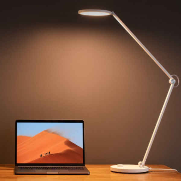 Desk lamp on a wooden surface with a laptop displaying a desert scene.