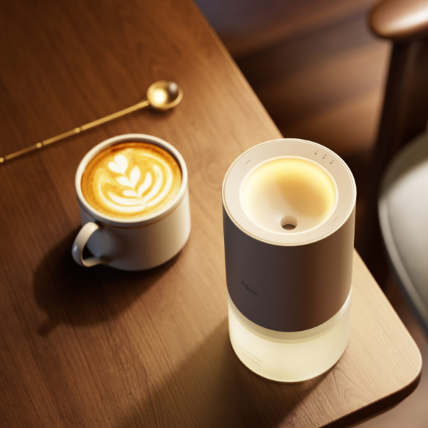 Cup of coffee with latte art next to a small lamp on a wooden surface