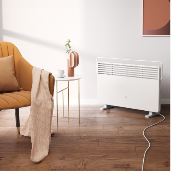 White electric radiator on a wooden floor with a chair and table in a room.