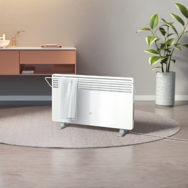 White electric radiator on a wooden floor with a plant and cabinet in the background
