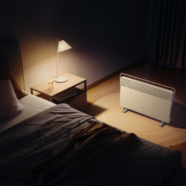 Room with a bed, nightstand, lamp, and convector heater in a dimly lit setting.