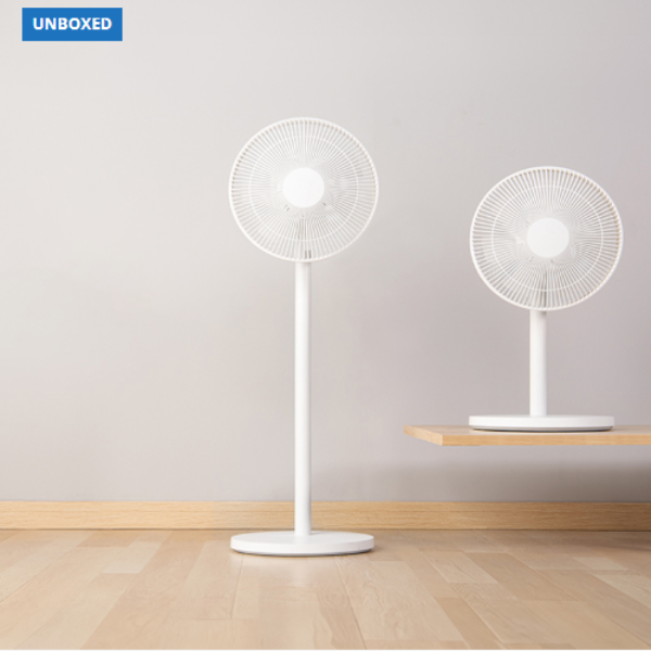 Two white table fans on a wooden floor with a plain wall background