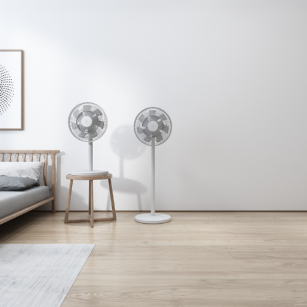 Two standing fans in a minimalistic room with a bed and wooden stool.