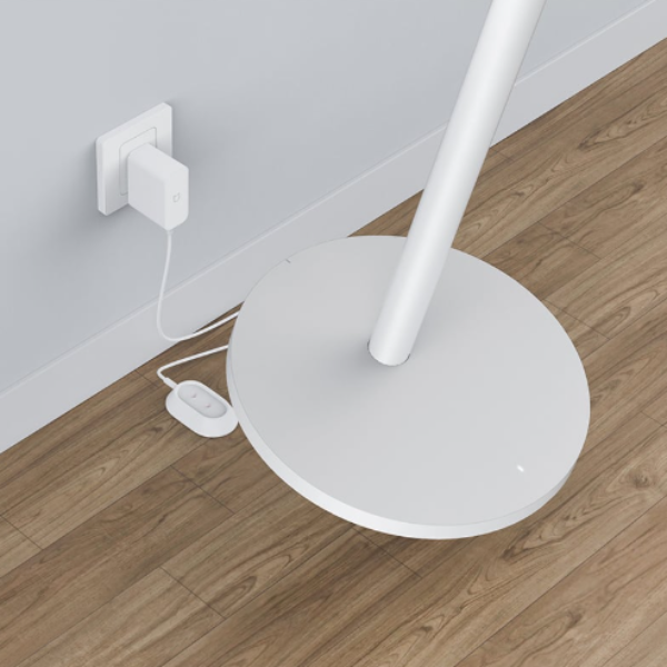 White floor lamp on a wooden floor with a power outlet in the background