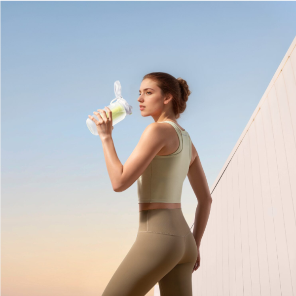Woman in athletic wear holding a water bottle against a clear sky.
