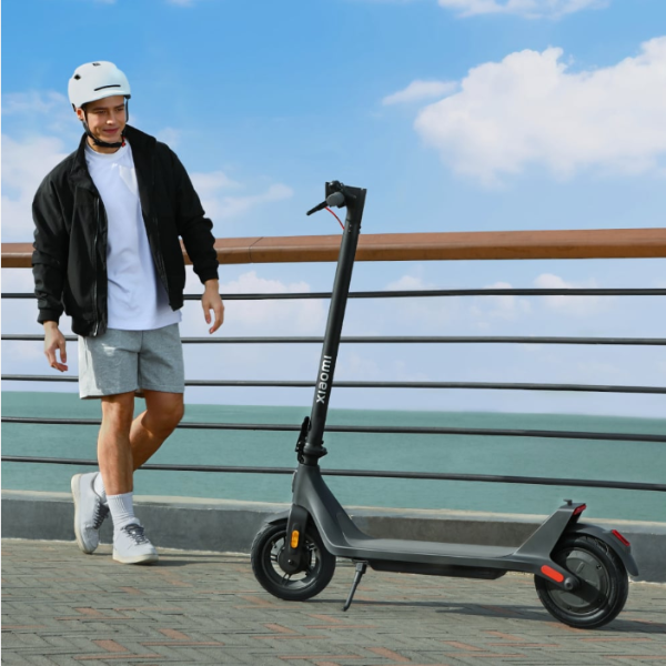 Person with a helmet standing next to a Xiaomi electric scooter by a waterfront.