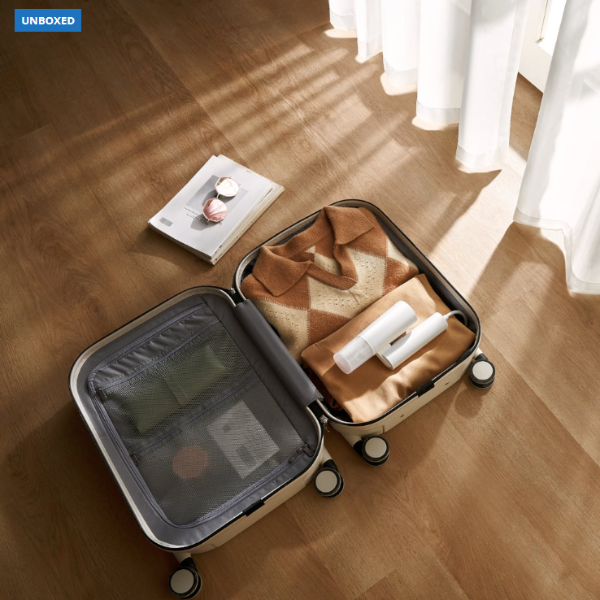 Open suitcase on a wooden floor with clothes and a book inside, labeled 'UNBOXED'.