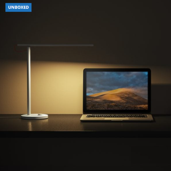 Desk lamp illuminating a laptop on a dark surface with 'UNBOXED' branding.