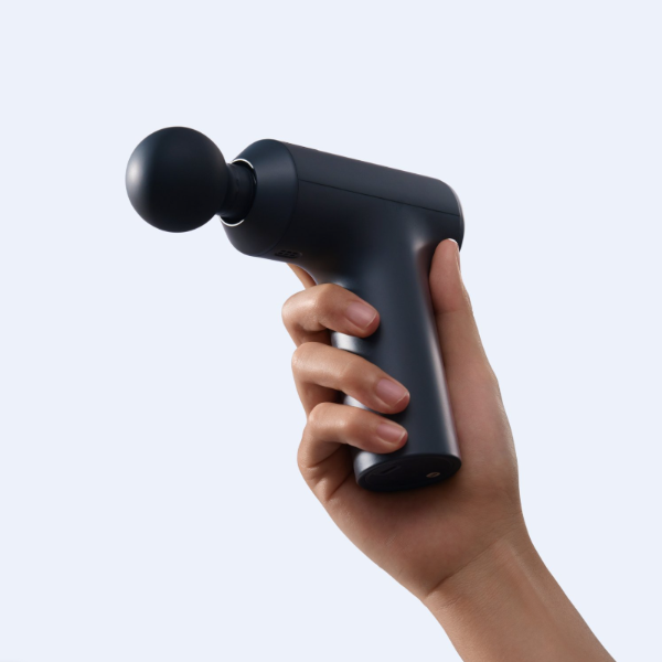 Hand holding a black massage gun against a light gray background