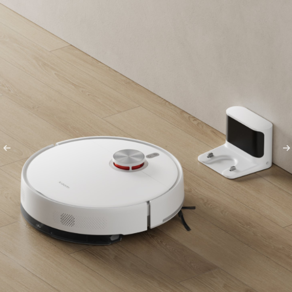 Robotic vacuum cleaner on a wooden floor with a wall-mounted device in the background