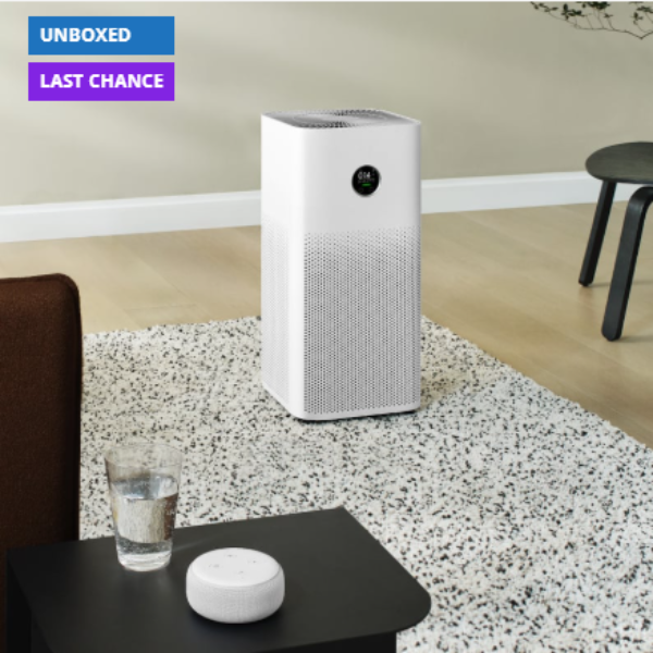 Air purifier on a speckled floor with a glass of water and a white device on a table.
